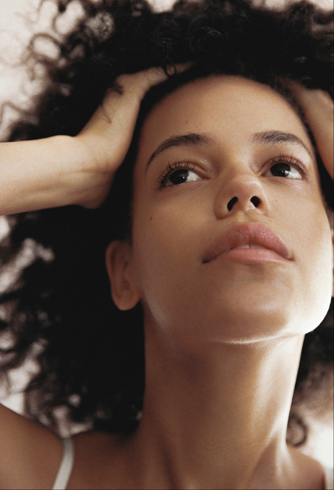Woman with curly hair touching her head against a neutral background