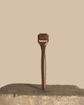 A dark brown derma roller tool standing upright on a rough stone surface against a solid beige background.