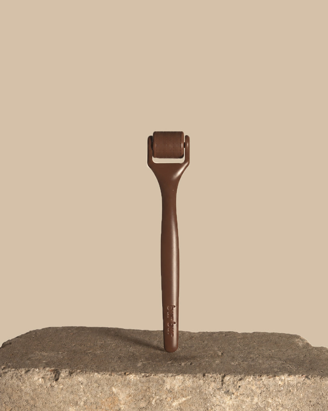 A dark brown derma roller tool standing upright on a rough stone surface against a solid beige background.