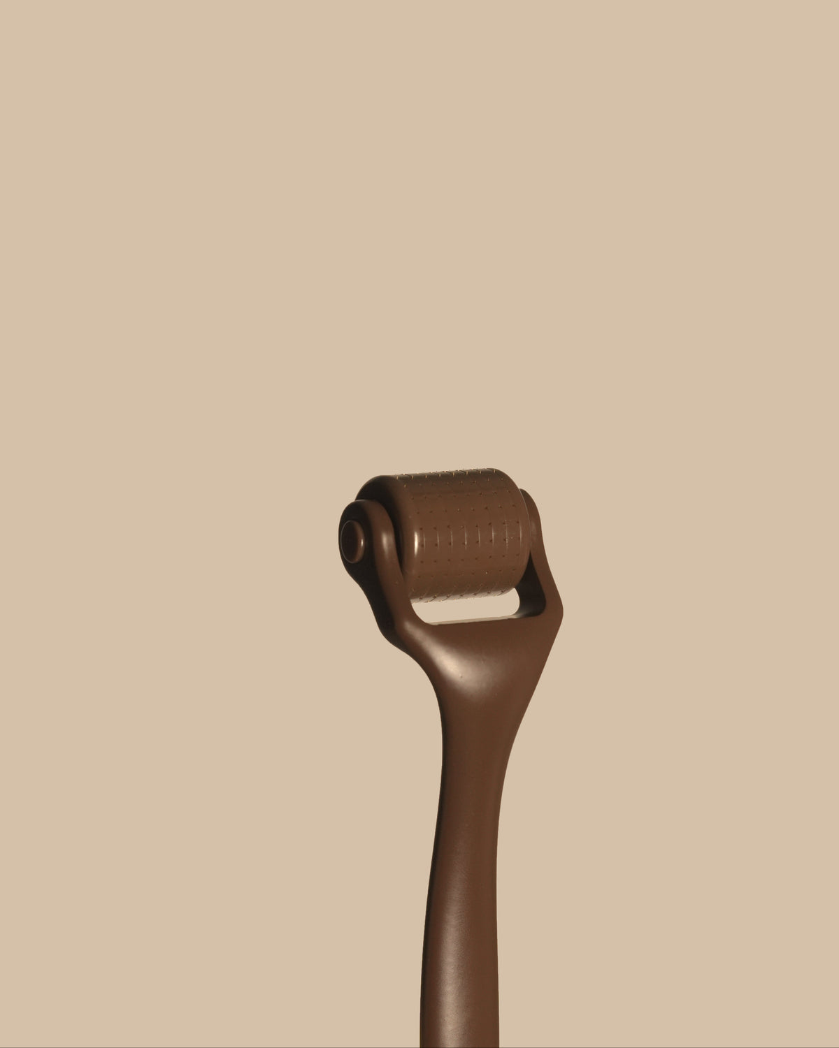 A close-up of a dark brown derma roller tool against a solid beige background.