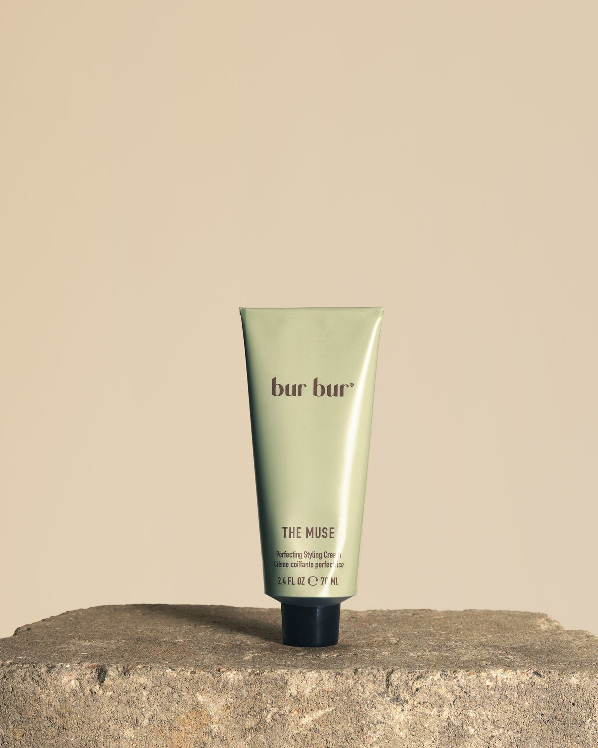 A squeeze tube of bur bur The Muse hydrating gel cream standing upright on a rough stone surface against a solid beige background.